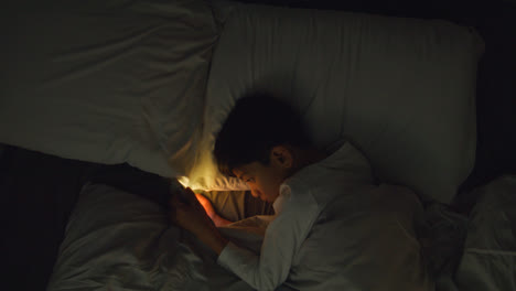 Young-Boy-In-Bedroom-At-Home-Lying-In-Bed-Using-Mobile-Phone-To-Text-Message-At-Night-1